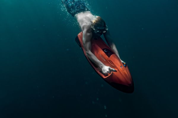 homme utilisant un scooter sous marin orange qui descend vers les profondeurs aquatiques